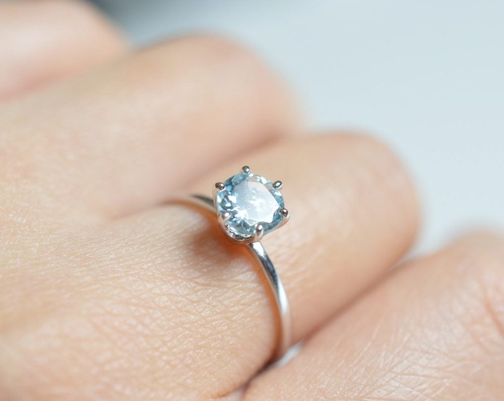 a blue aquamarine stone set in white gold with six prongs on a hand